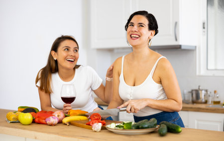 Happy young lesbian couple drinking wine and cooking dinner in kitchenの写真素材