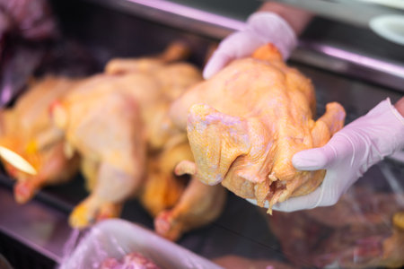 Row chicken held in hands by seller against background of showcase of butcher shopの写真素材