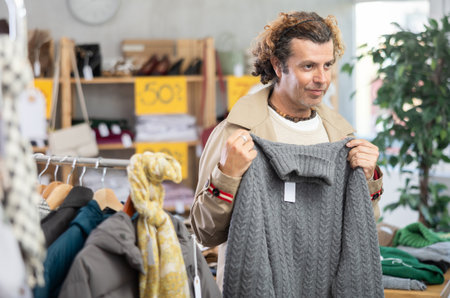 man stands near the counter with clothes and chooses a sweaterの写真素材