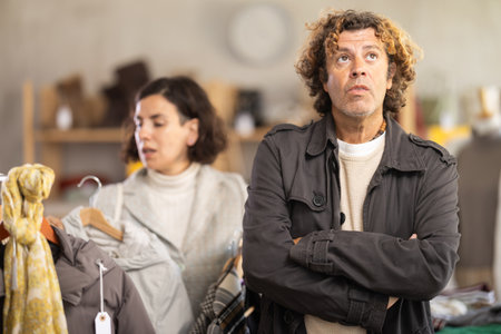 European female customer choose new jacket or coat for winter season, man bored while waiting for woman in clothing storeの写真素材