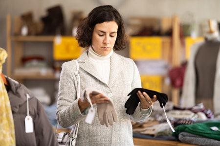 Focused female client choosing warm gloves for winter season in clothing storeの写真素材