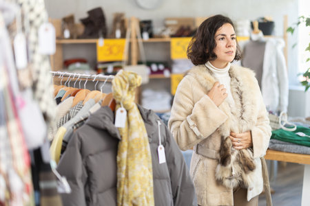 Beautiful interested lady standing in clothing shop and trying new fur coat for winter seasonの写真素材