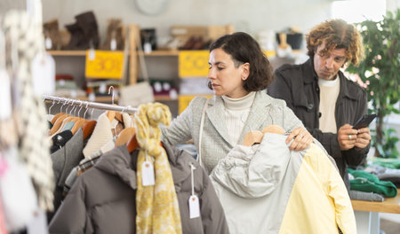 Woman choosing jackets and coats next to man with phone