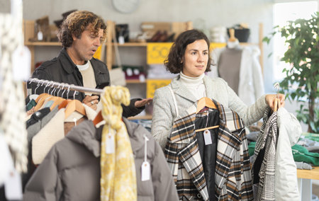 Woman choose jacket in store, husband accompanies his wife during shoppingの写真素材