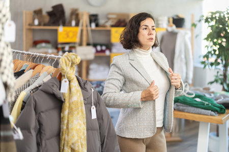 Interested woman selecting and trying new blazer for winter season in clothing shopの写真素材