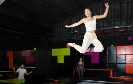 Girl acrobatic athlete jumping and exercising on trampoline indoors, modern hobby and fitness...