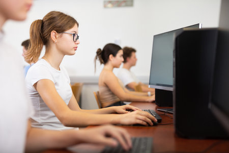 Focused female student in glasses using PC and studying computer science in the classroomの写真素材