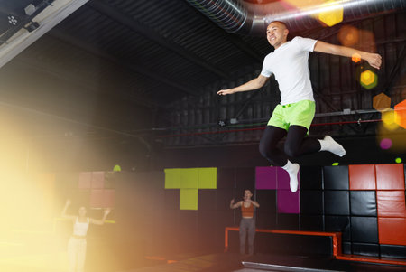 Fitness, fun, leisure and sport activity concept - happy man jumping on trampoline indoorsの写真素材