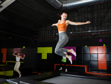 Enthusiastic woman leaping at vibrant trampoline gym with friendsの写真素材