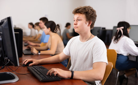 Side view on concentrated teenager male student sitting at desk, preparing for exam in computer classの写真素材