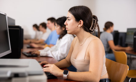 Side view on focused teenager female student sitting at desk in computer class, preparing for examの写真素材