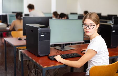 Young girl student turned around and looking at camera during lesson in computer classの写真素材