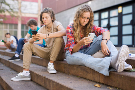Boy and girl playing on smartphones during recess between college classes closeupの写真素材
