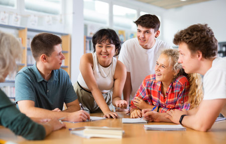 Group of schoolchildren discussing together in library and preparing for examの写真素材