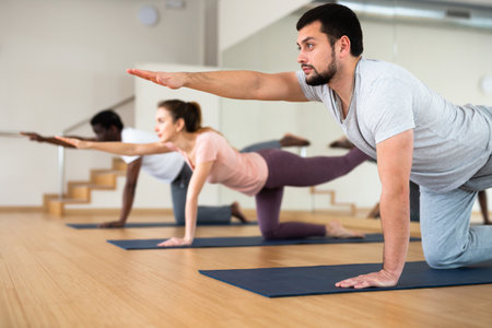 Man doing bird dog exercise with other people in gymの写真素材