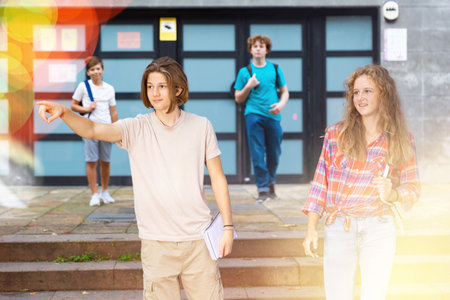 Students walk out of college doors. Guy points hand at someoneの写真素材