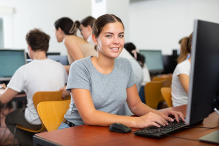 Smiling young woman sitting in computer room at workplace and looking at cameraの写真素材