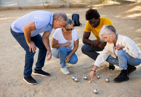 Multiracial mature adult people measuring distance between balls in petanque game outside in a parkの写真素材