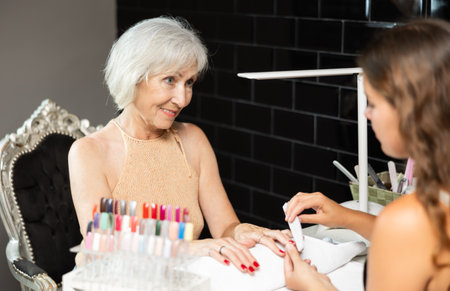 Unrecognizable girl manicure master files nails and performs grooming procedure for senior womanの写真素材