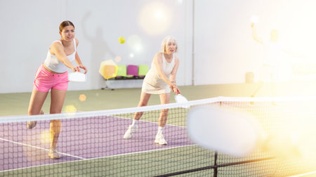 Young girl playing doubles pickleball match with aged female partnerの写真素材