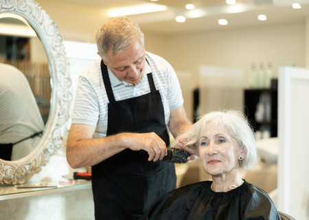 Professional male hairdresser cuts hair of elderly woman at beauty salonの写真素材