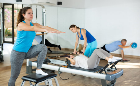 Sportive young female exercising on Pilates chair during group workout in fitness studioの写真素材