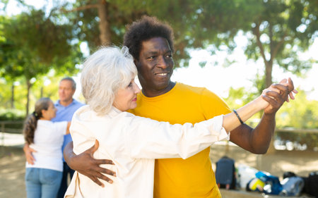 Happy positive mature multinational pensioners spending time together and dancing in pairs outdoorsの写真素材