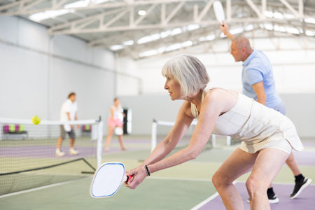 Positive elderly woman playing pickleball on indoor courtの写真素材