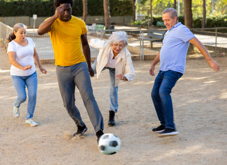 The football team of positive elderly diverse people having football activity on a sandy area in autumn afternoons in parkの写真素材