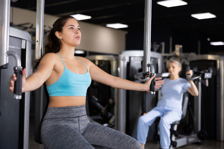 Active young woman training at chest fly machine in gym
