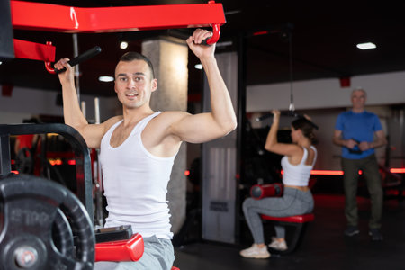 Portrait of man doing triceps curls in exercise machine during strength training in gym