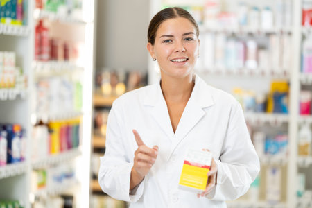 Female consultant pharmacist holds box in hands and offers to purchase remedy to alleviate conditionの写真素材