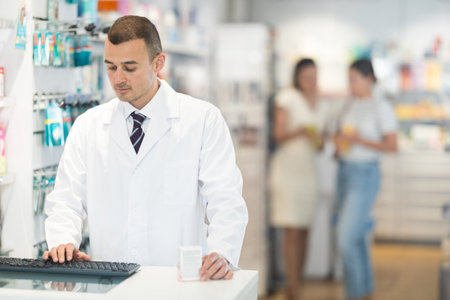 Male pharmacist looking for medicine using computerの写真素材