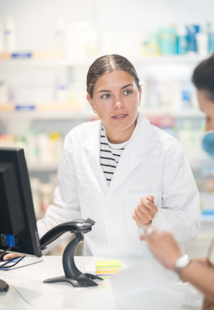 Young female pharmacist speaking to woman customer buying medicinal preparation in drugstoreの写真素材