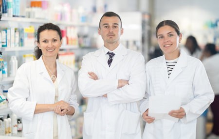 Three pharmacists in white doctors robes posing together in chemists shopの写真素材