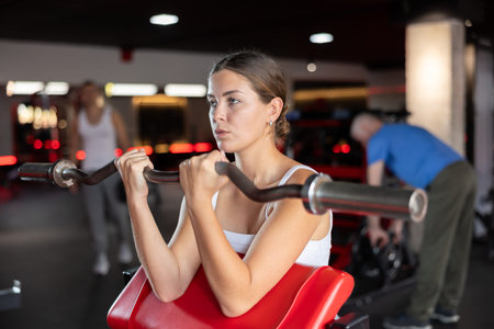 Sporty girl performing set of exercises with barbell during intense workout. Concept of weight...