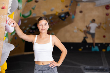 Slender girl in sportswear is standing near climbing wall in gymの写真素材