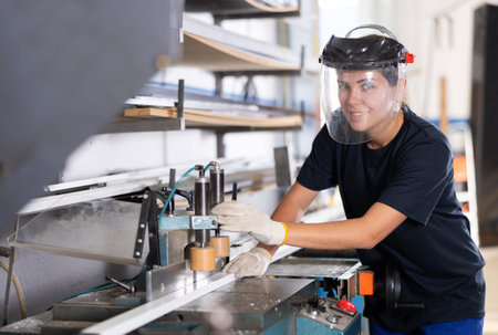 Positive workwoman cutting PVC profile on industrial machine in workshop