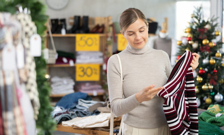 Uncertain young woman choosing sweater in clothing storeの写真素材