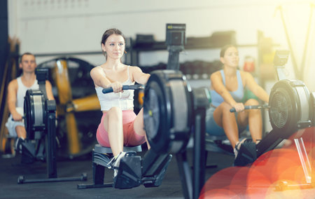 Athletic woman in sportswear training on rowing machine in sport gym