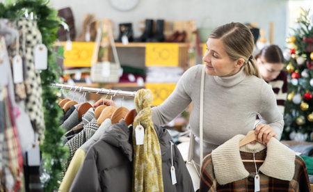 Adult woman carefully choosing outerwear among jackets and coatsの写真素材