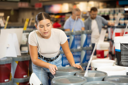 Girl examine bucket of paint, buy collect necessary supplies for renovationの写真素材