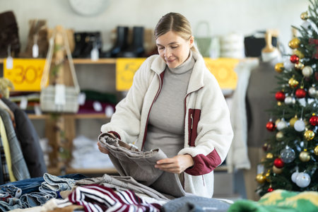 Woman client looks at products in store, choose closely ladies trousersの写真素材