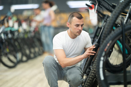 Attentive buyer examining wheel and gear mechanism of bicycle in storeの写真素材