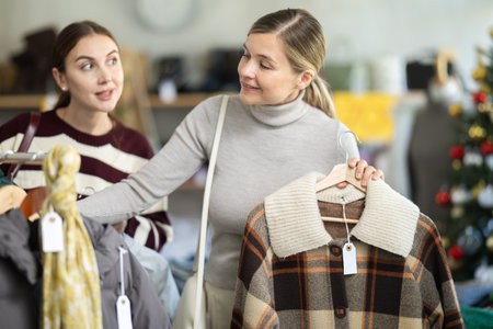 Two women client looks at products in store, choose closely winter down coat or jacketの写真素材