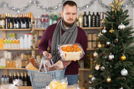 Middle-aged guy choosing tangerines in a Christmas-decorated storeの写真素材