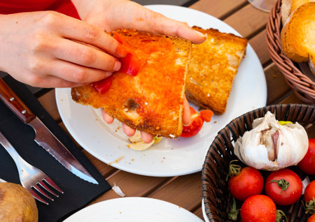 Womans hand rubs surface of slice of bread with half ripe tomatoの写真素材