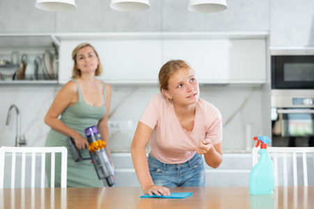 Dreamy teenage girl engaged in household cleaning with motherの写真素材