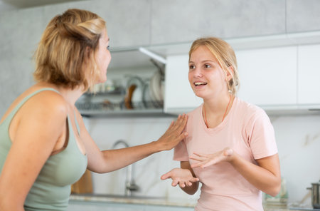 Cheerful teenage daughter talking friendly to mother in kitchenの写真素材