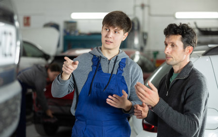 Young man car mechanic talks with man client in workshop and takes order.の写真素材